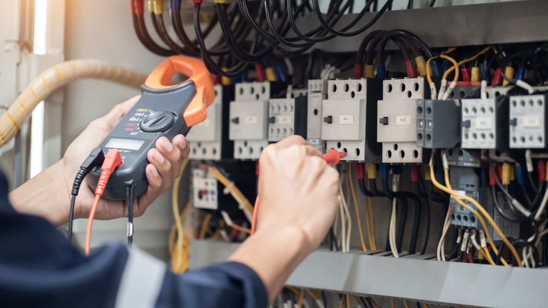 Electrician using clamp meter to test electrical panel with circuit breakers