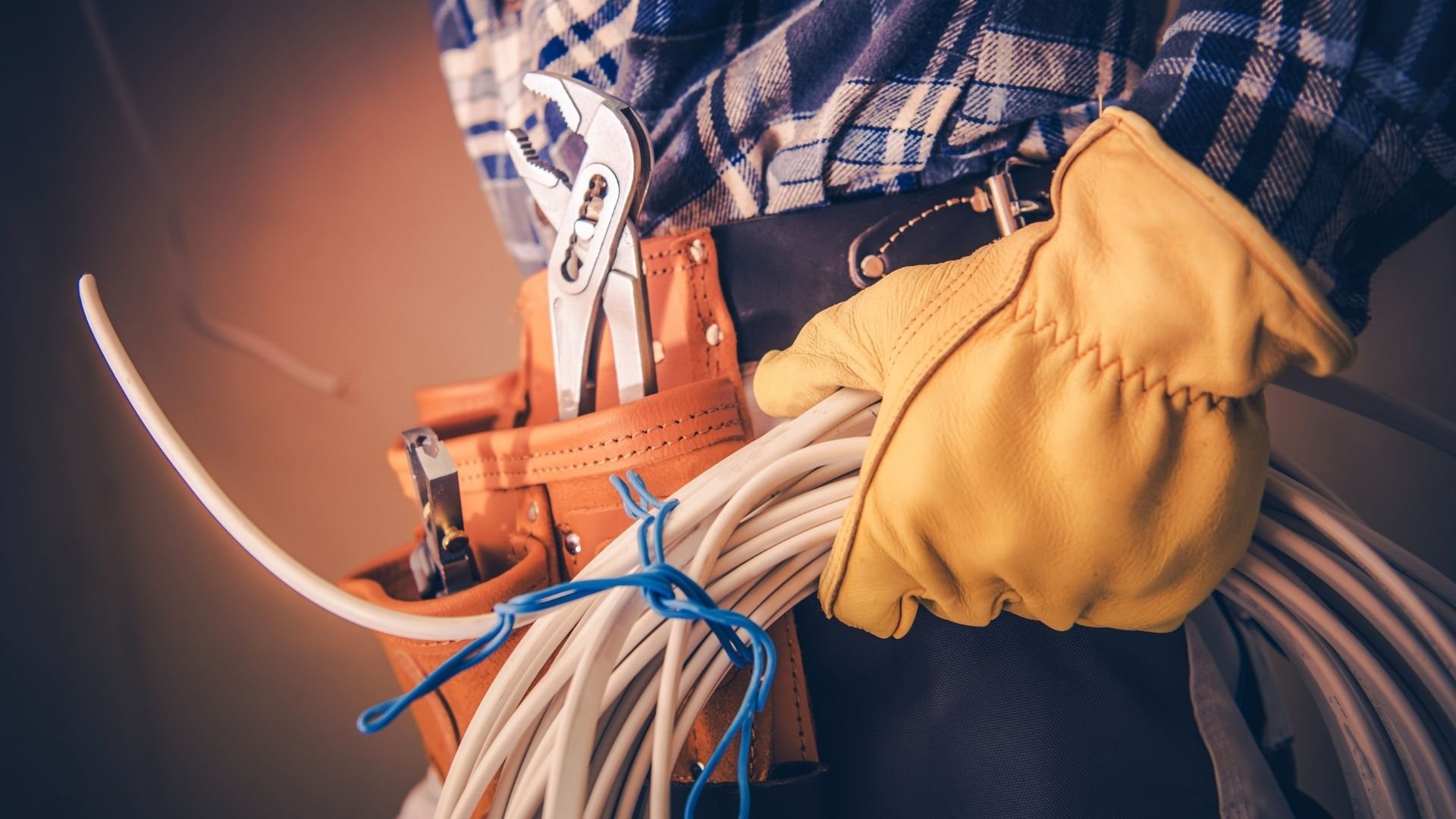 Worker holding wrench and coiled rope from orange tool belt