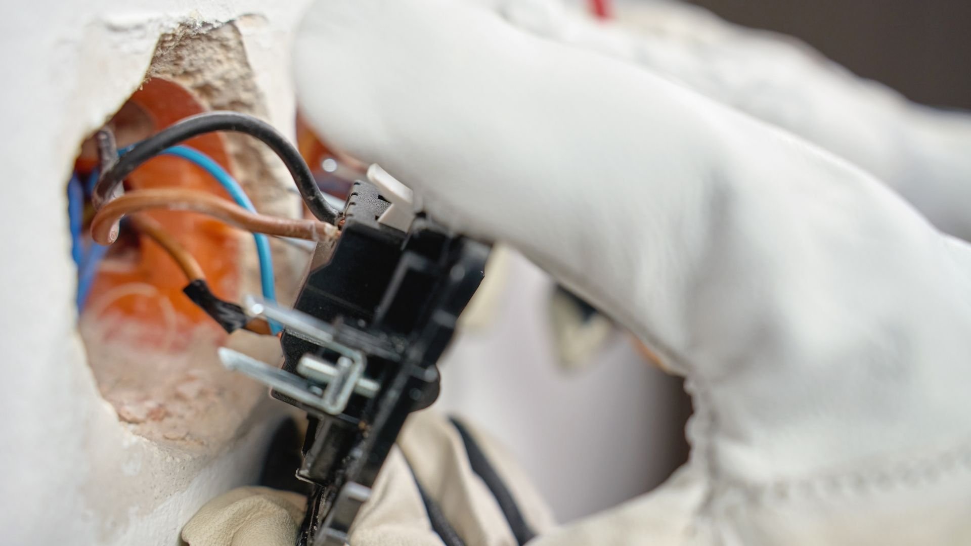 Close-up of electrical wiring with orange and blue wires connected to black terminal block