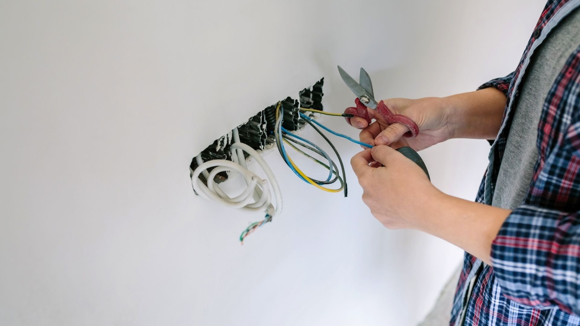 Person using red pruning shears to cut colored electrical wires from wall outlet
