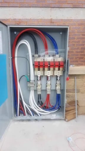 Plumbing manifold with red, white, and blue pipes and valve connections on brick wall.