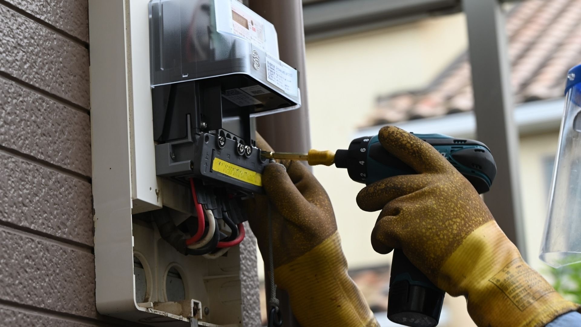Technician in work gloves installing or maintaining an electric meter on building exterior wall.