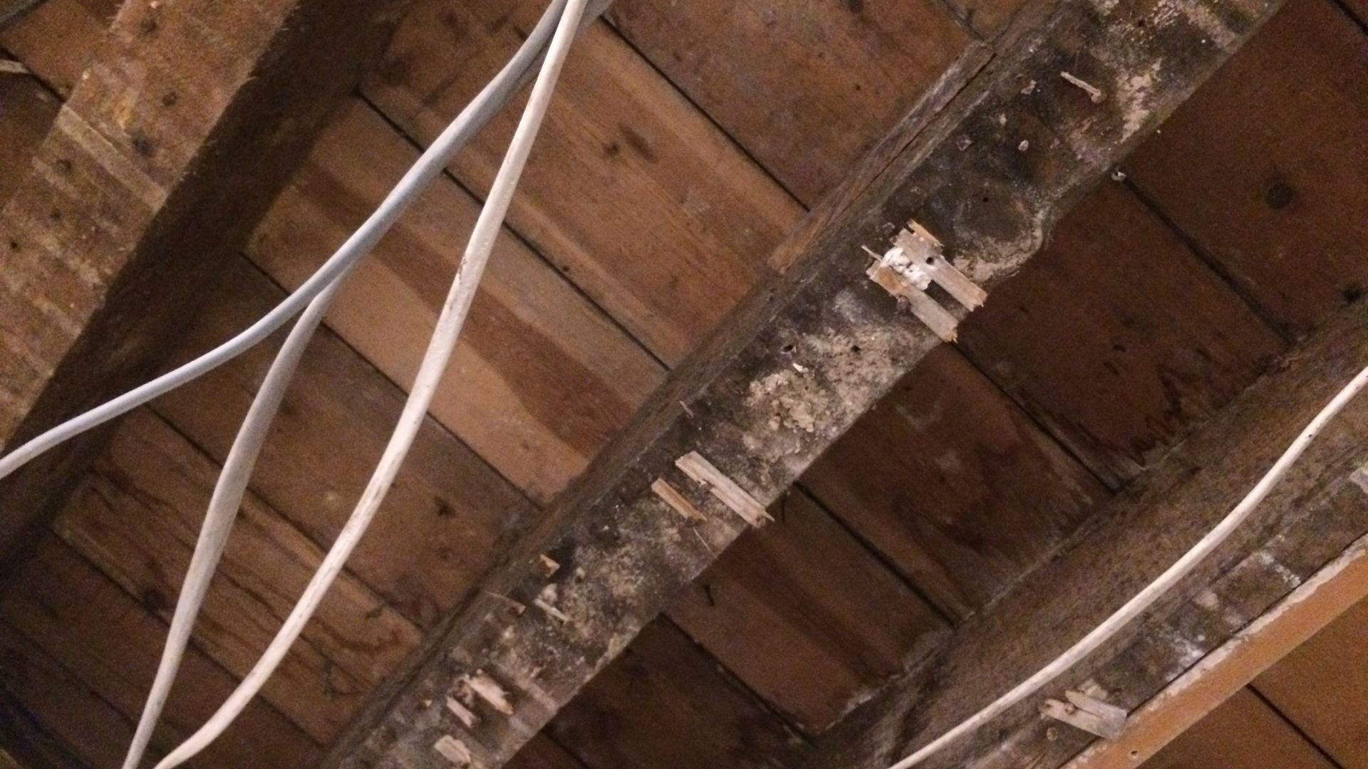 White PVC pipes on weathered wooden ceiling with beams and electrical fixtures