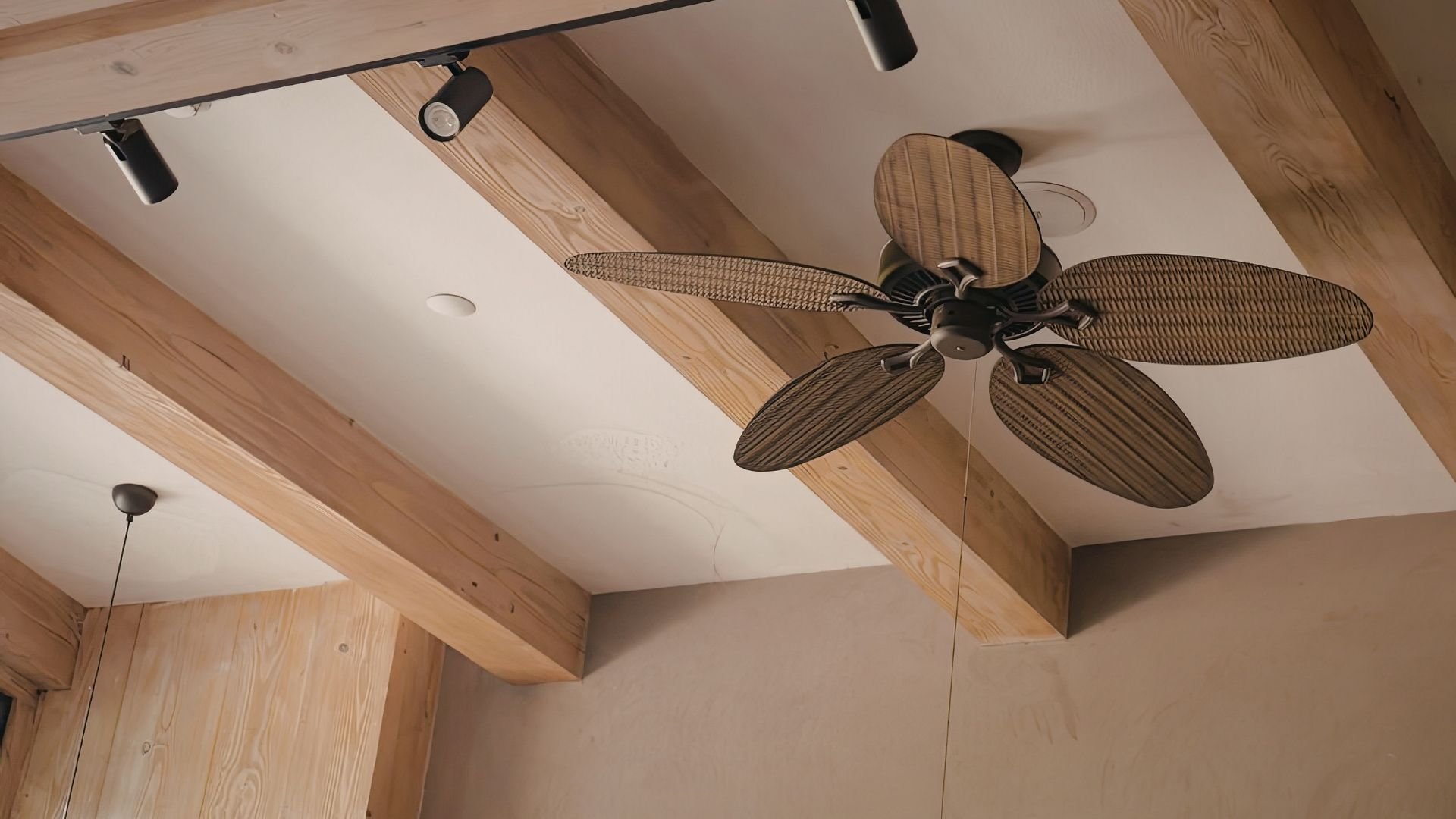 Ceiling fan with woven leaf blades mounted on wooden beam in modern interior space.