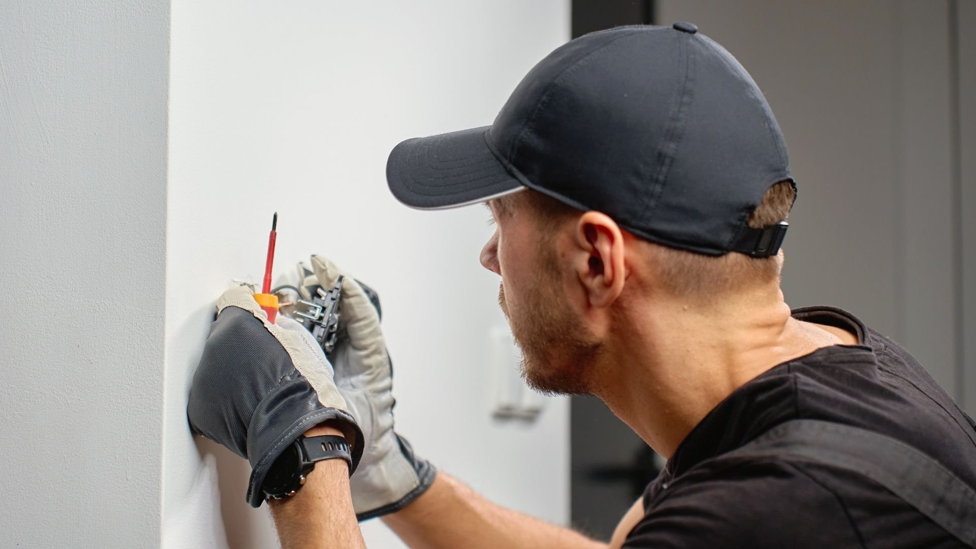 Worker wearing black cap and gloves marking wall with red pencil and measuring tool