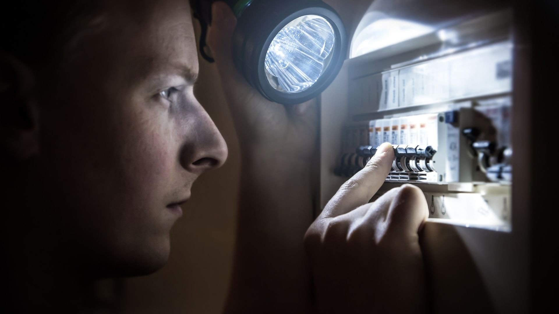 Electrician inspecting electrical panel with headlamp at night