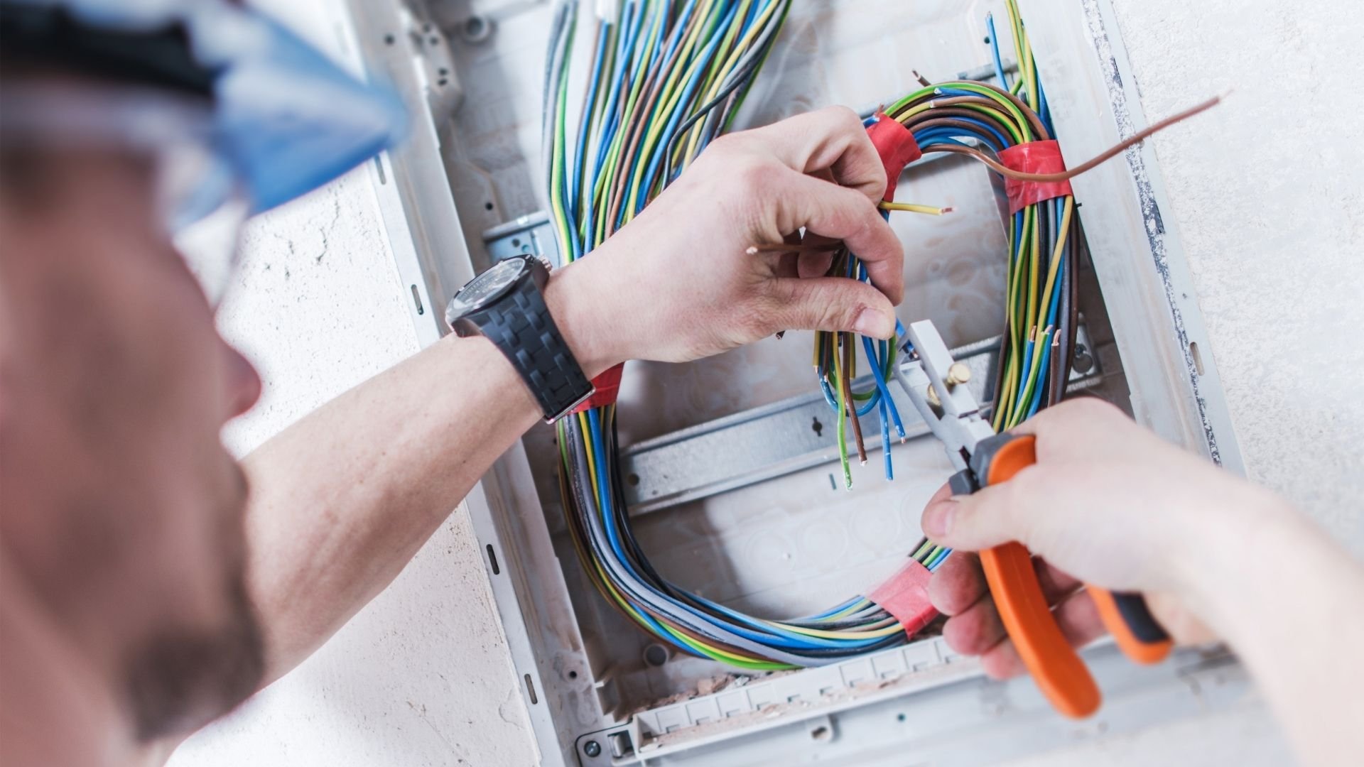 Electrician installing and organizing colorful electrical wires with connectors in panel box.