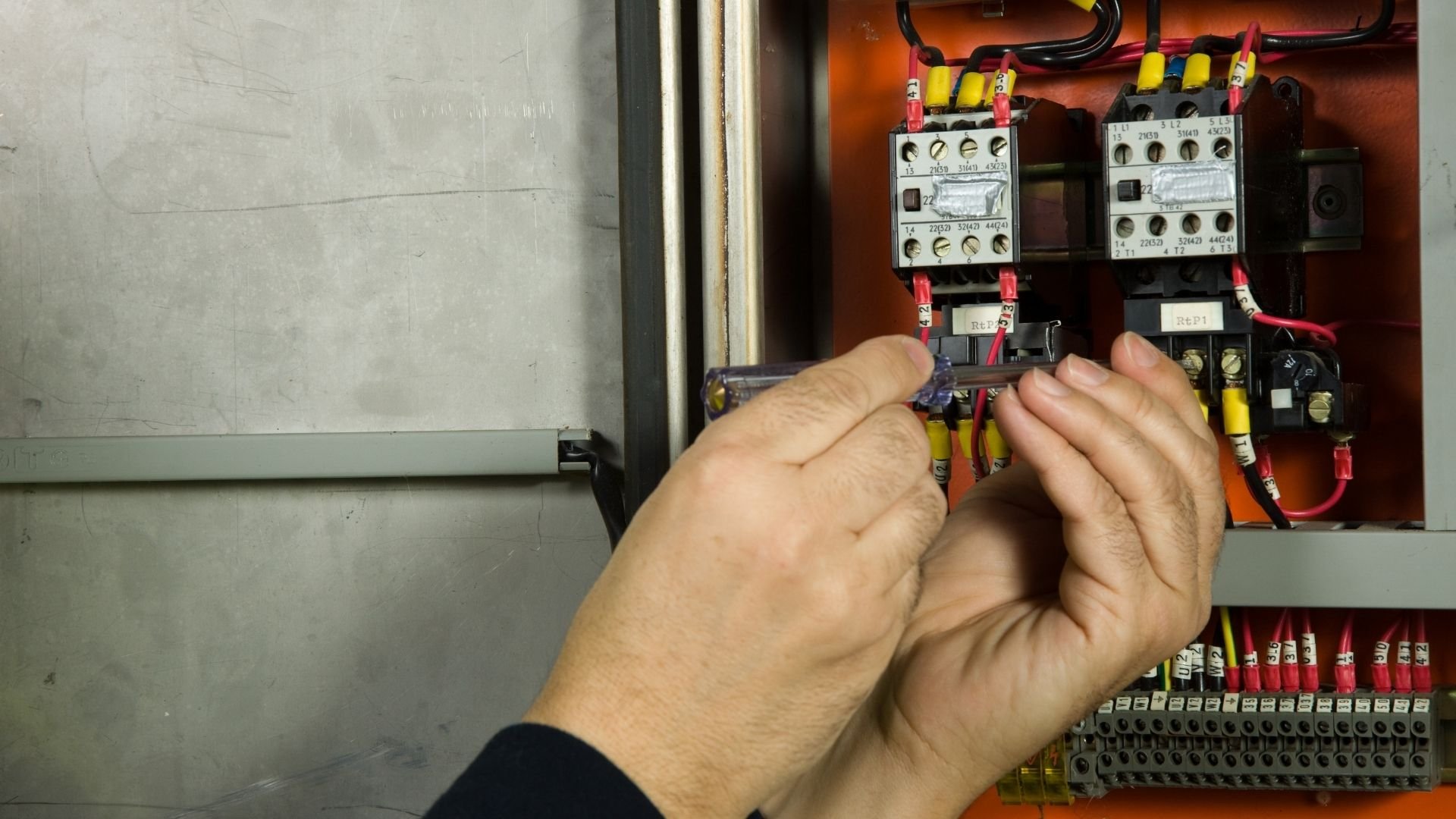 Electrician working on industrial electrical control panel with relays and wiring