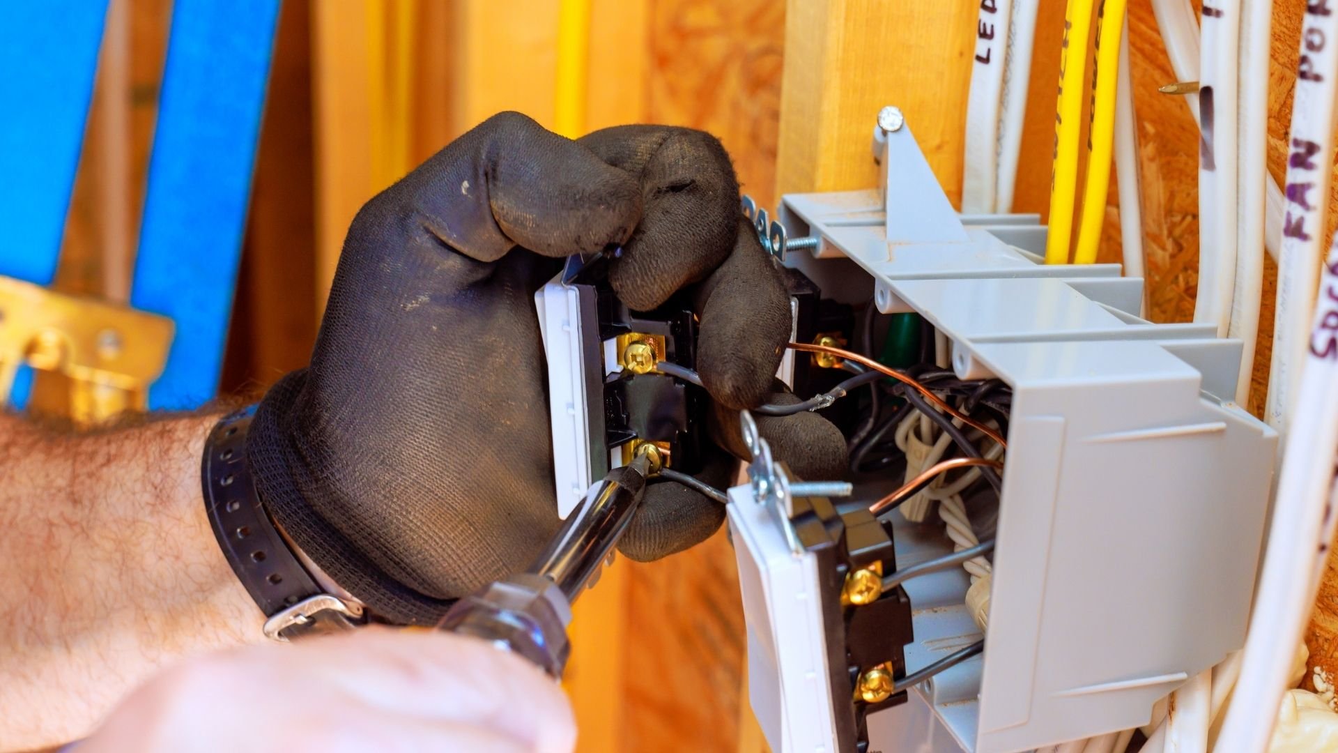 Gloved hand installing electrical wiring in a circuit breaker panel with yellow background.