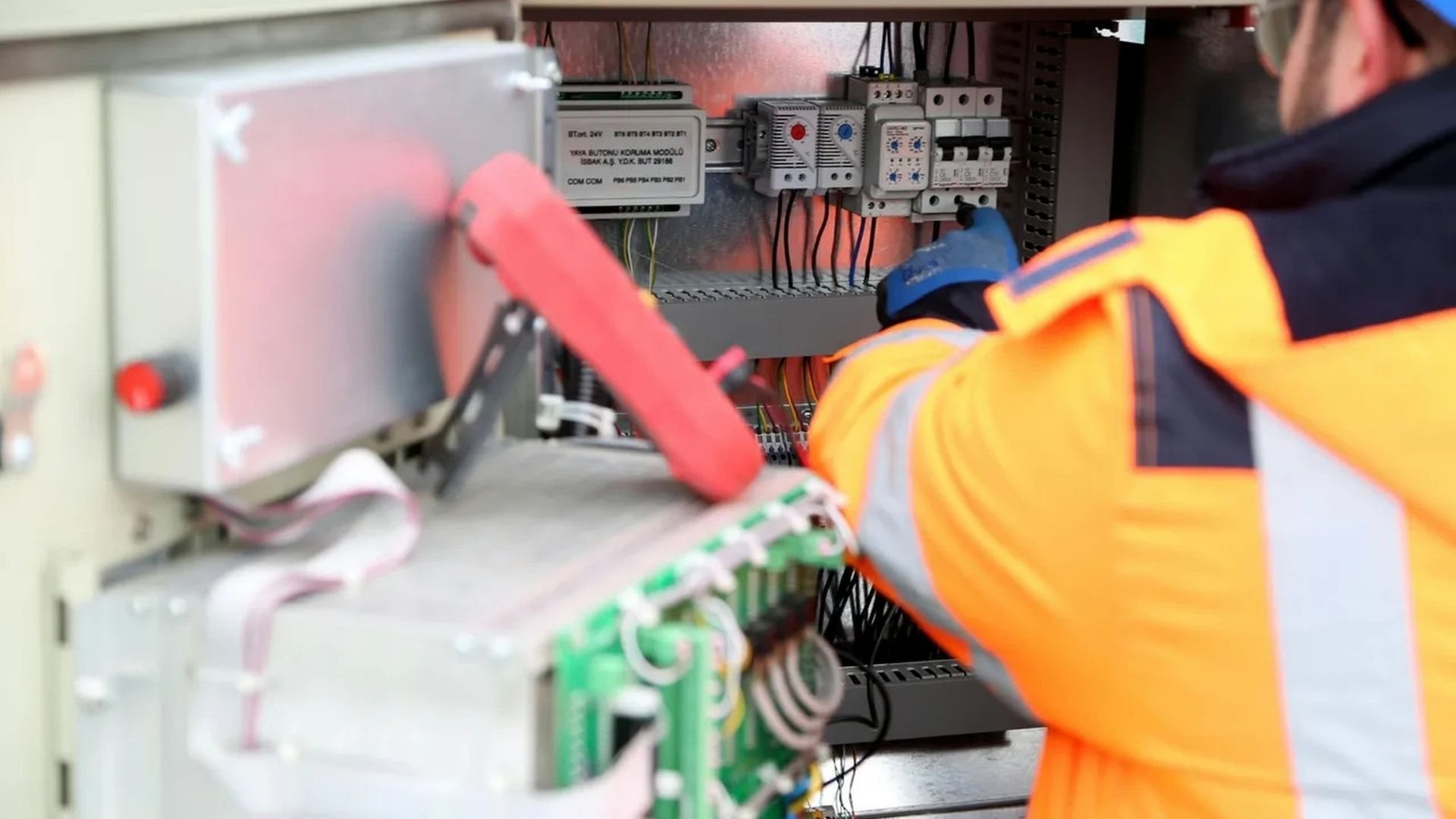 Electrician in safety gear inspecting industrial electrical panel with wires and switches